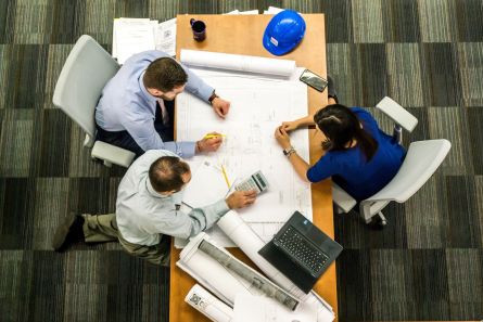 Three People Sitting Beside Table, Plans And Hardhat on Table